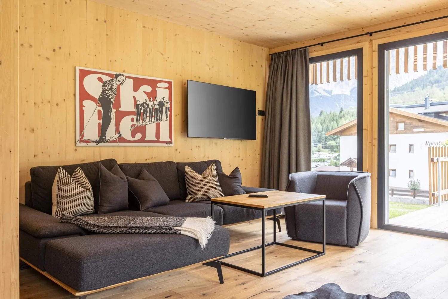Moderner Wohnbereich mit dunklem Sofa, Holzverkleidung und Bergpanorama