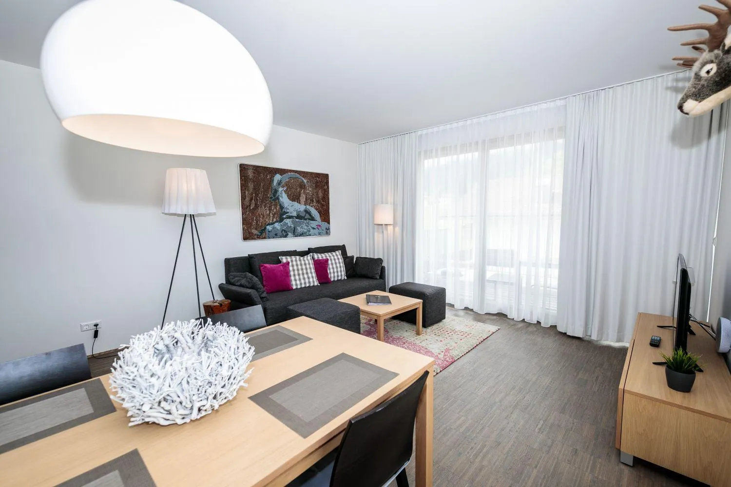 Wohnzimmer mit dunklem Sofa, Esstisch und Gämsenbild an der Wand