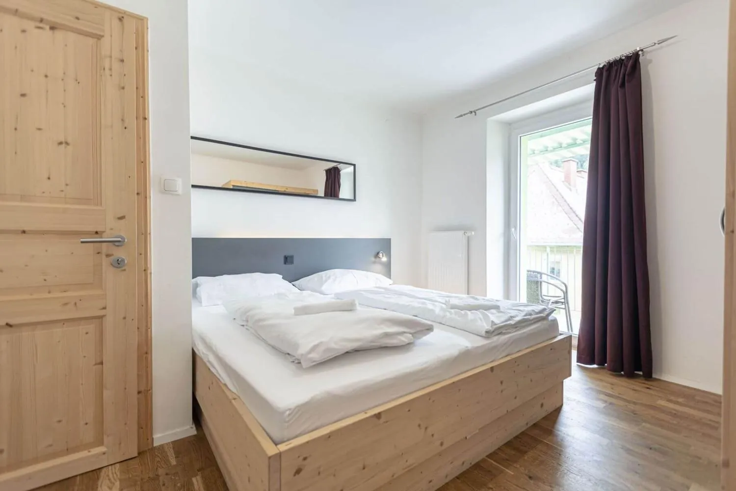 Modernes Schlafzimmer mit Holzbett, grauem Kopfteil und Fenster