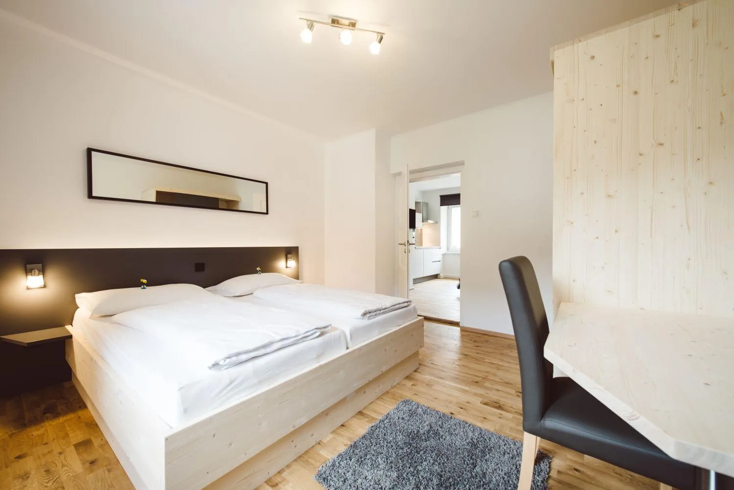 Helles Schlafzimmer mit Holzbett, weißen Kissen und grauem Teppich