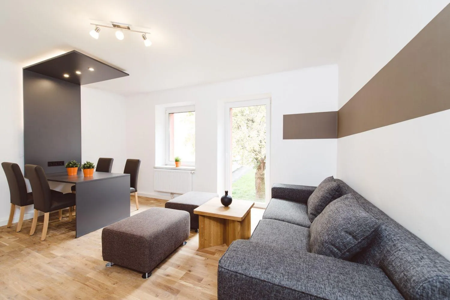 Hell eingerichtetes Wohnzimmer mit grauem Sofa, Esstisch und modernem Design