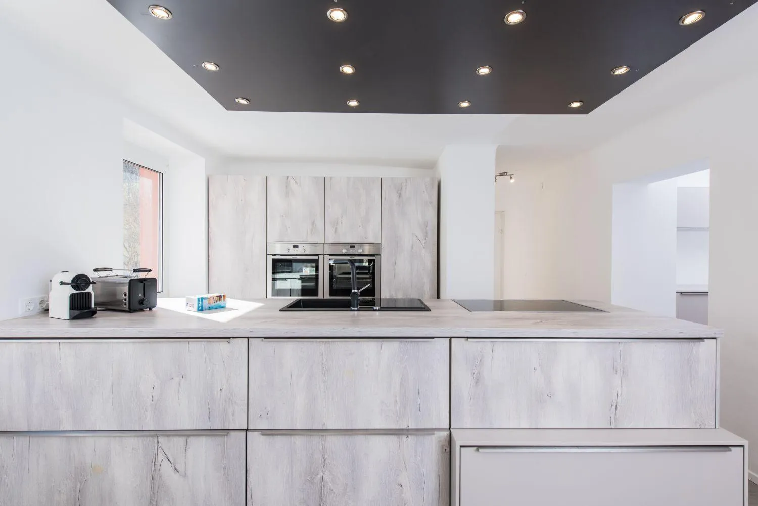 Moderne Küche mit weißem Küchenblock, grauem Hängeelement und LED-Deckenleuchten