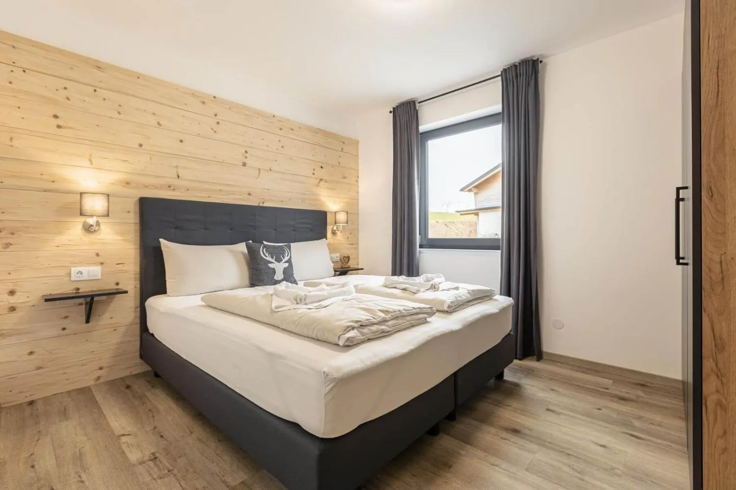 Schlafzimmer mit Holzwand, schwarzem Bett und Balkonzugang