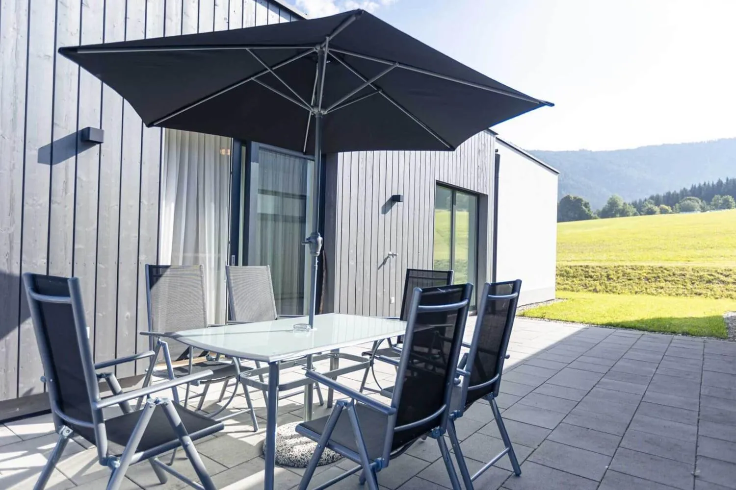 Terrasse mit Sitzgruppe und großem Sonnenschirm vor Bergkulisse