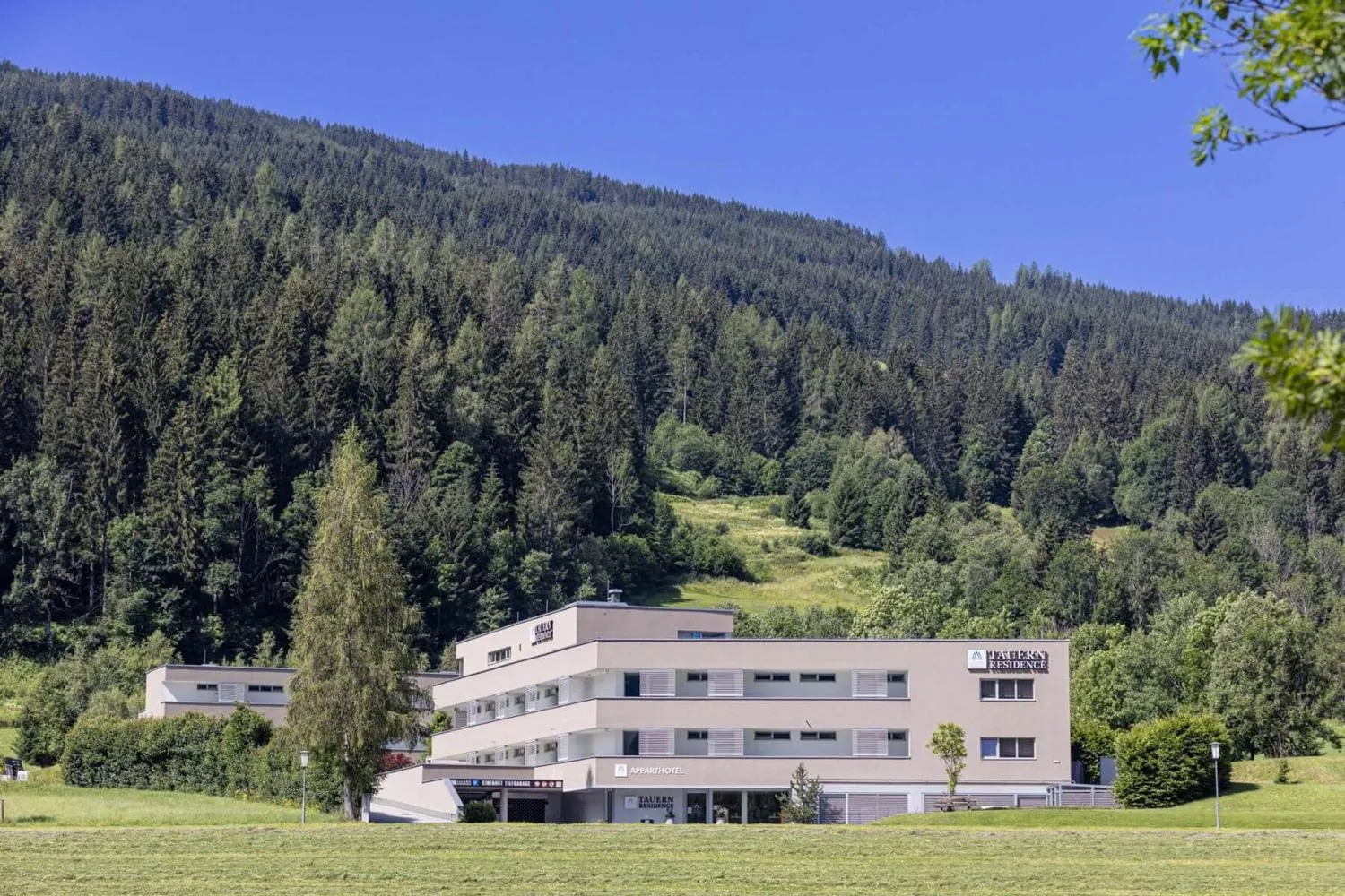 Aparthotel in grüner Sommertallandschaft umgeben von Nadelwäldern