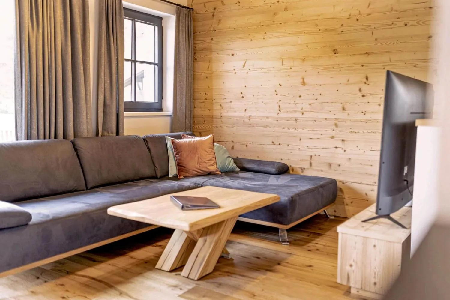 Holz-Wohnraum mit schwarzem Ledersofa, Fenster und TV-Ecke