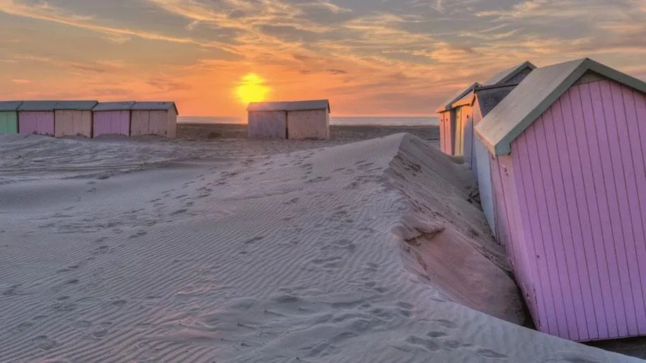 Bunte Strandkabinen bei Sonnenuntergang über Sandstrand und Meer