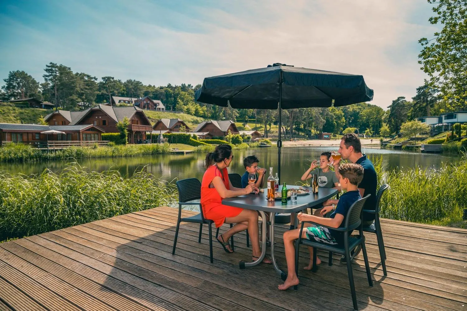 Familie beim Essen auf Holzterrasse mit Seeufer-Ausblick