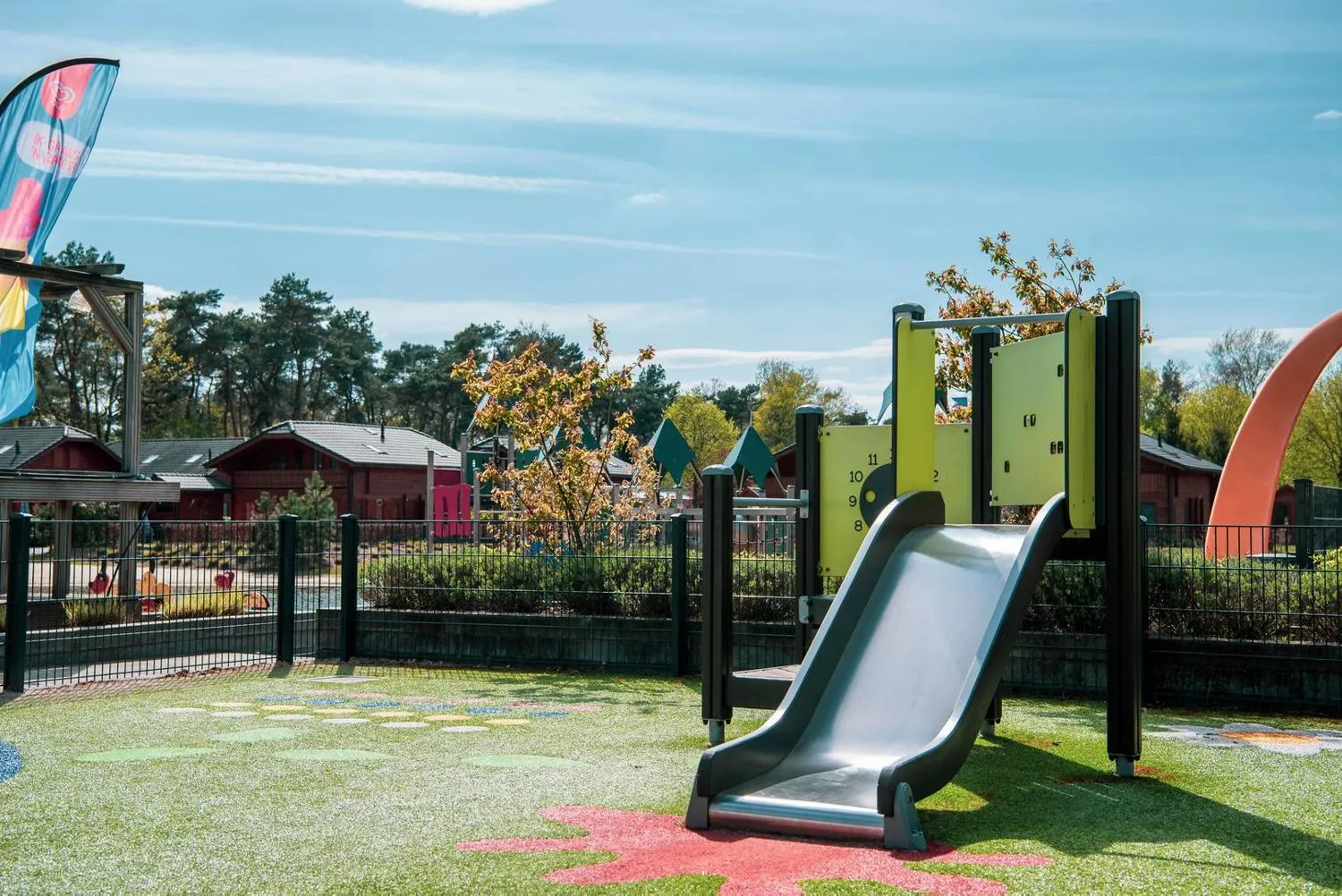 Moderner Kinderplatz mit Rutsche und Kletter-Struktur, Ferienpark-Häuser im Hintergrund