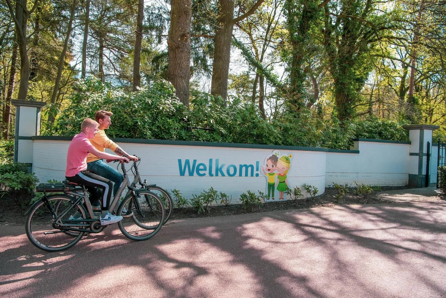 Willkommensschild am Ferienpark mit rotem Fahrweg durch Wald