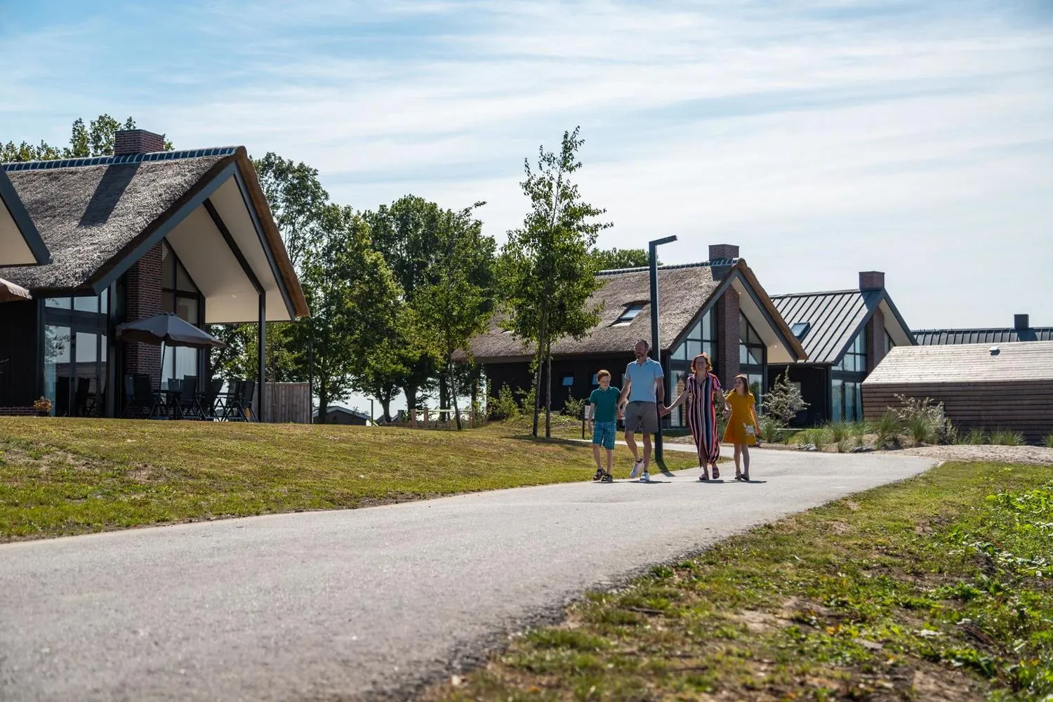 Moderne Häuser mit Strohdächern am Parkweg, Personen spazieren vorbei