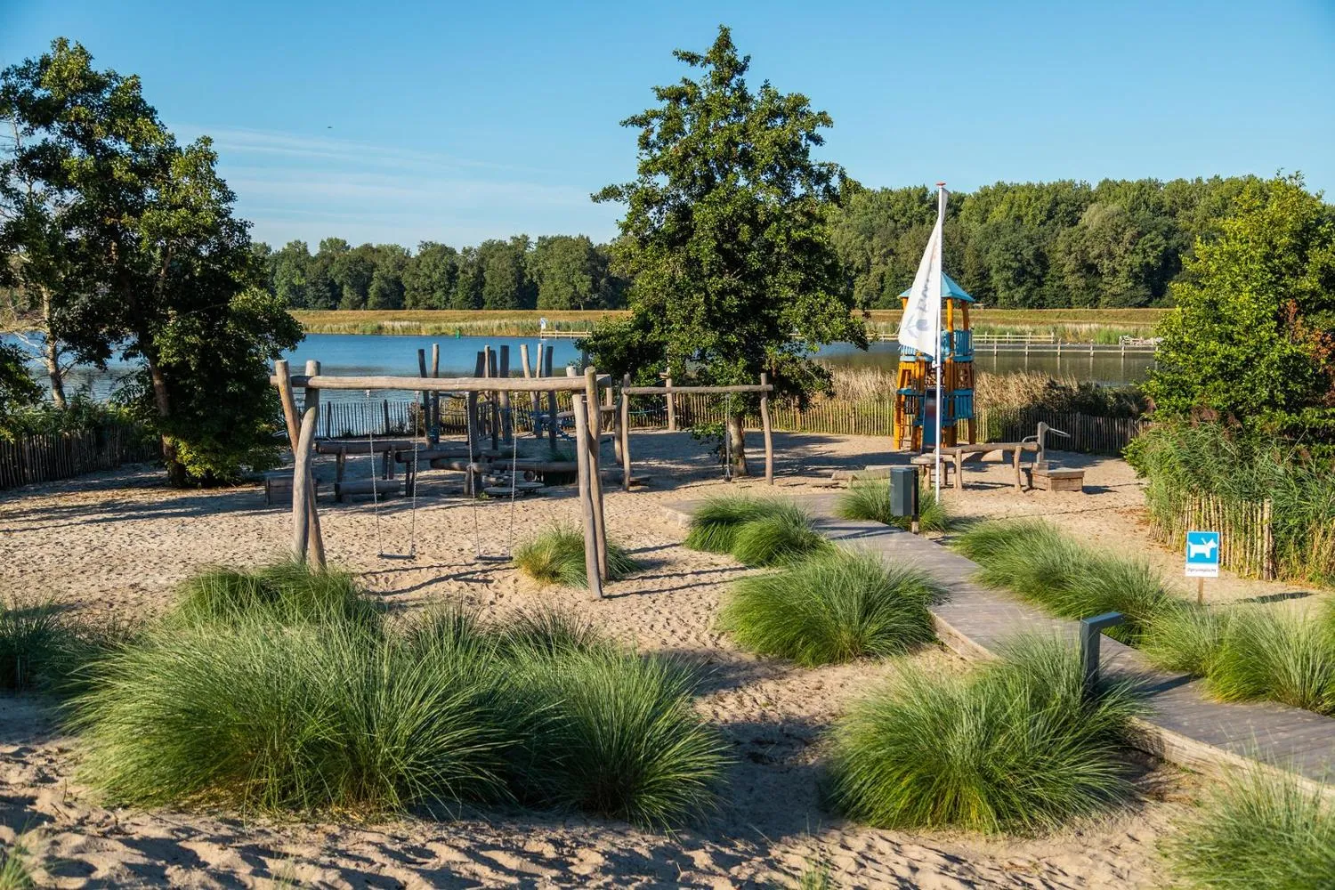 Spielplatz mit Schaukeln und Rutsche am Seestrand, Bäume im Hintergrund