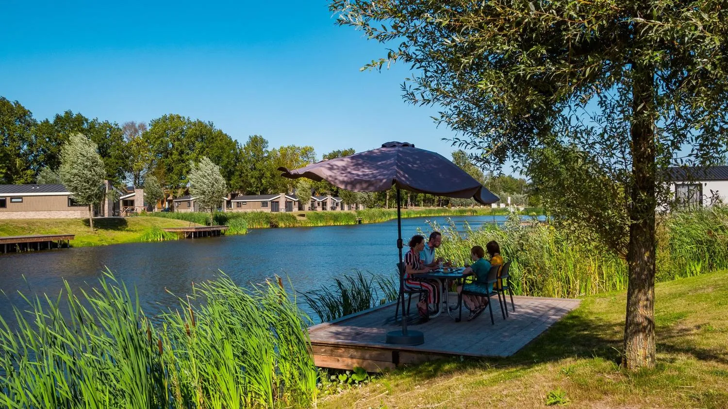 Essbereich mit schwarzem Sonnenschirm am See, Ferienhäuser im Hintergrund