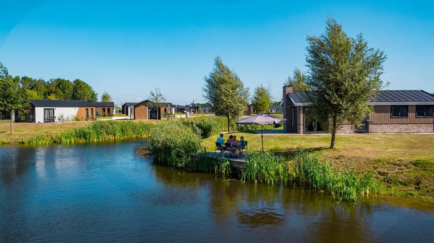 Ferienpark-Übersicht mit modernen Häusern, Personen unter Sonnenschirm am See