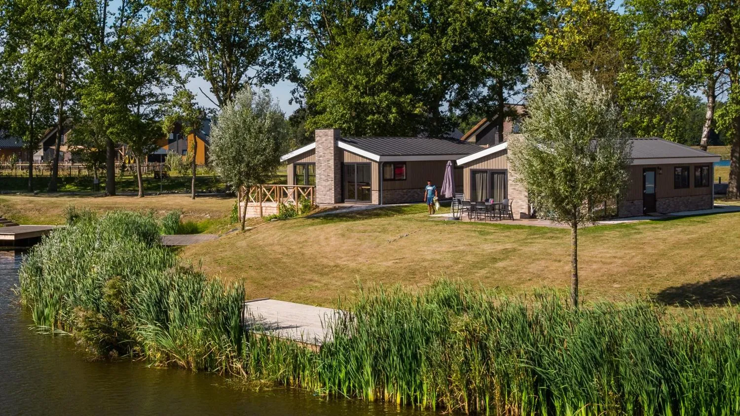 Modernes Ferienhaus mit Ziegelakzenten, Person auf Terrasse, Wiese am Wasser