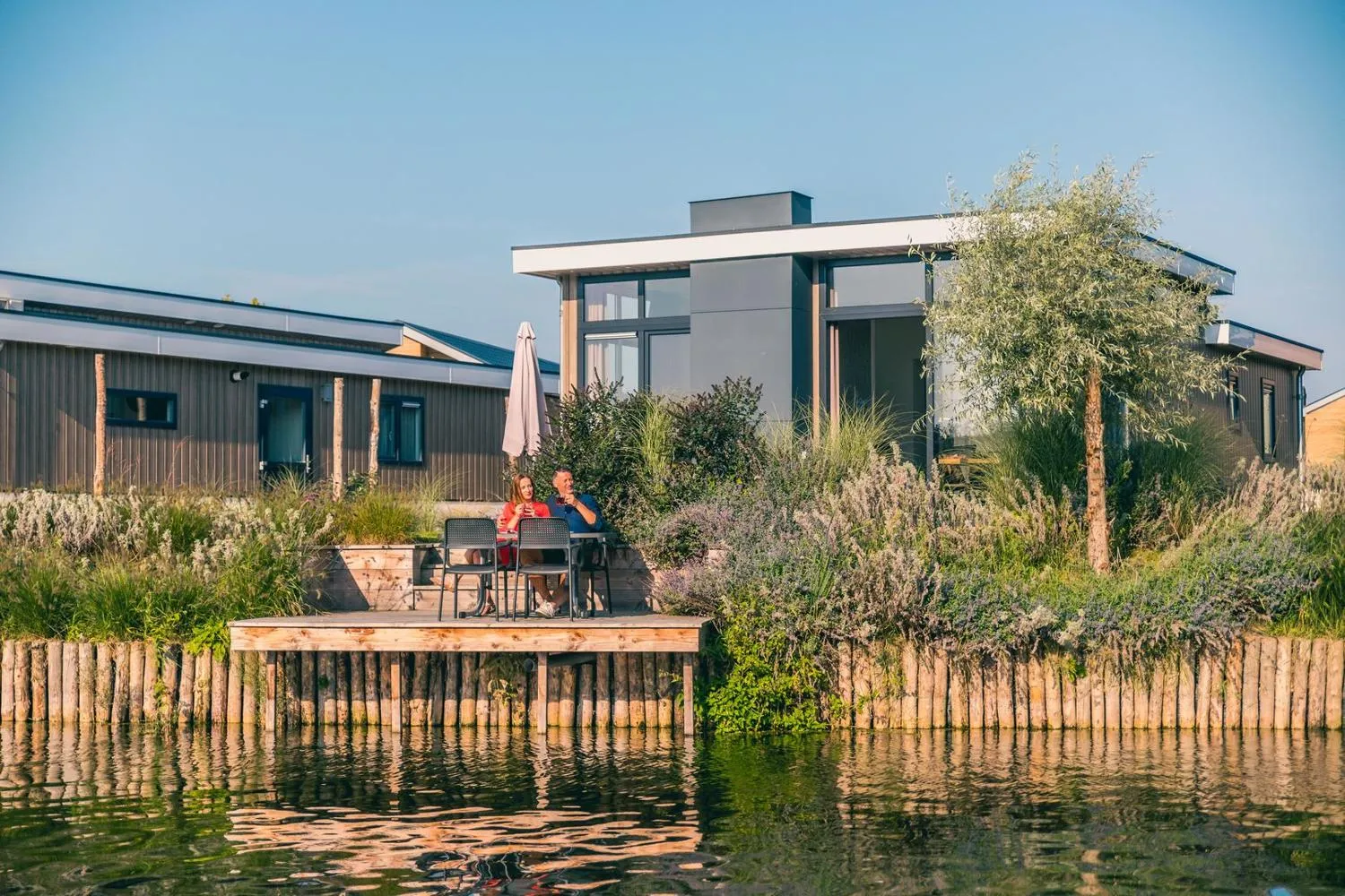 Gäste entspannen auf der Wasserfrontterrasse eines modernen Ferienhauses