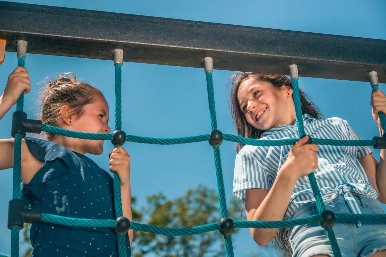 Zwei Mädchen klettern auf Seil-Gittergerüst am Spielplatz